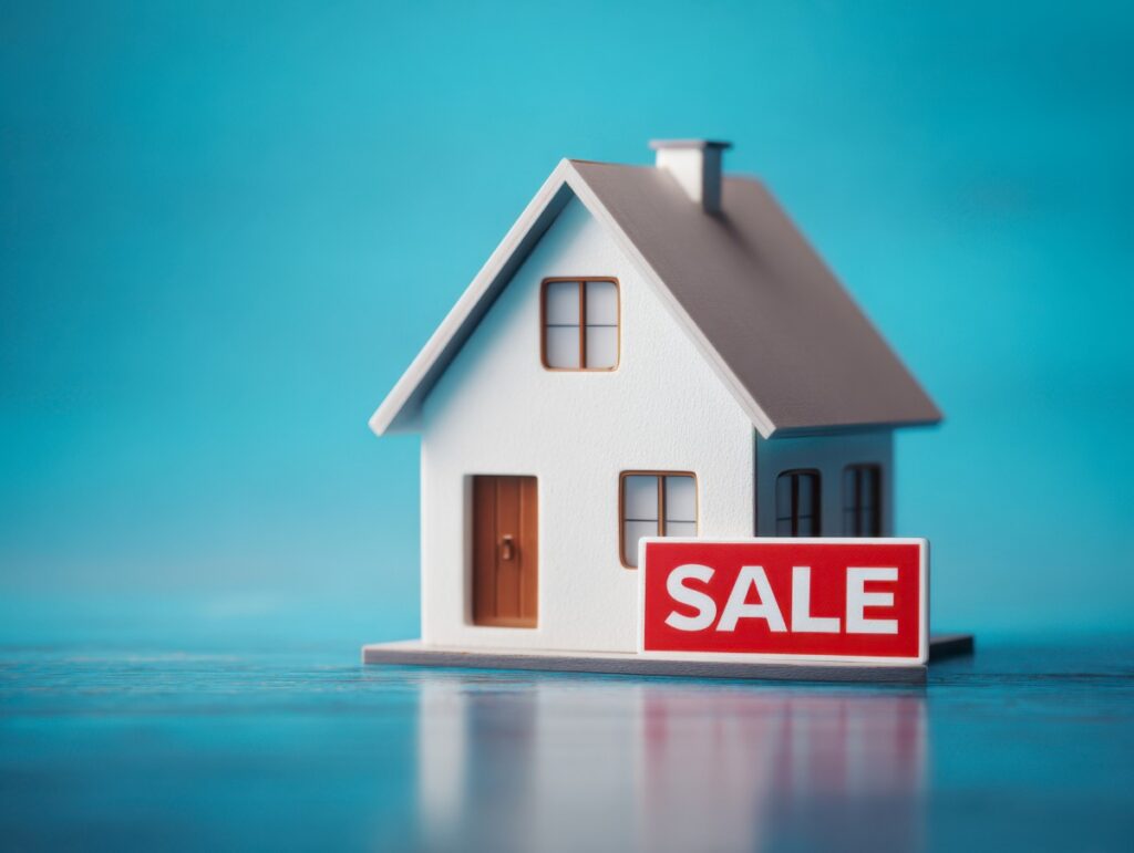 Small white model house with a red sale sign