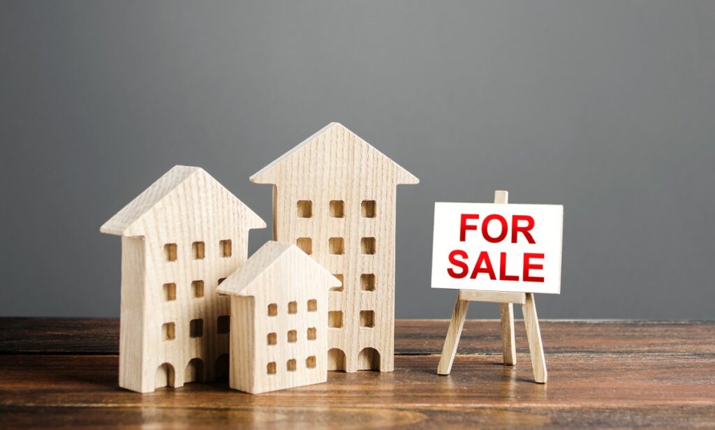 Wooden figures of residential buildings and an easel sign labeled for sale