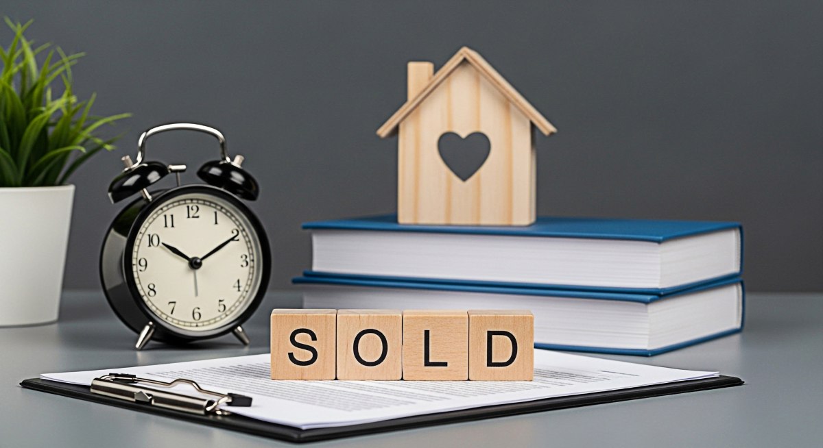 Real estate agent finalizing a property sale with a wooden house model alarm clock and SOLD blocks