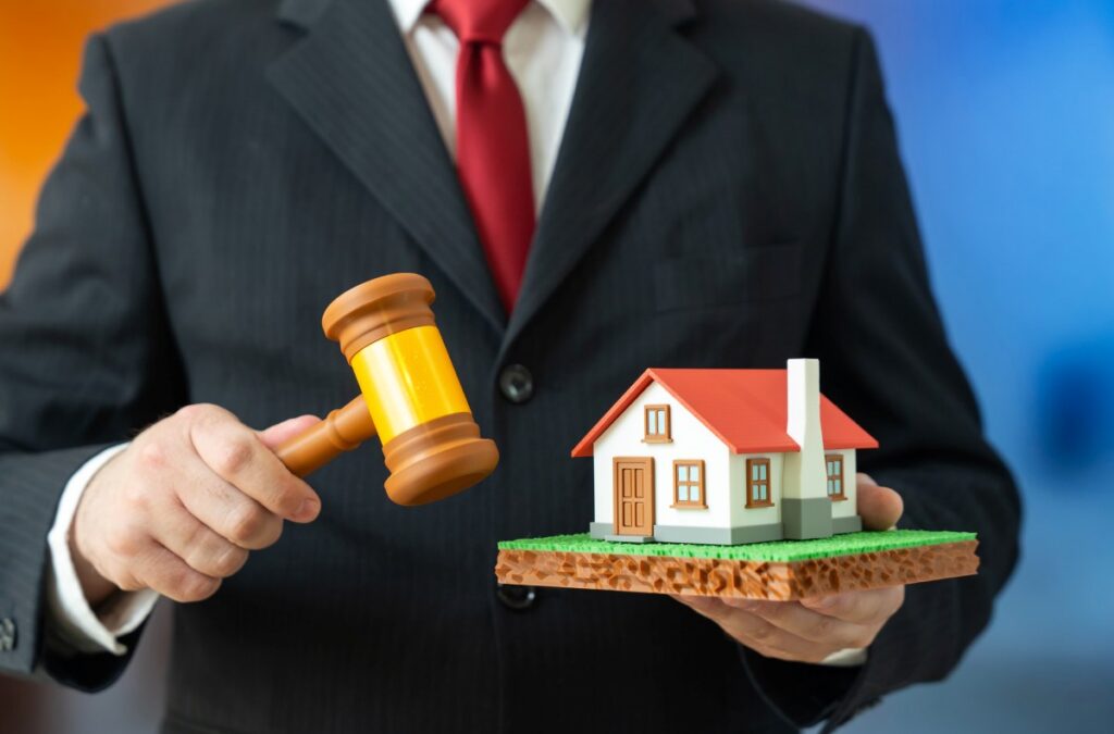A man holds a house and a judge's gavel. A real estate court order