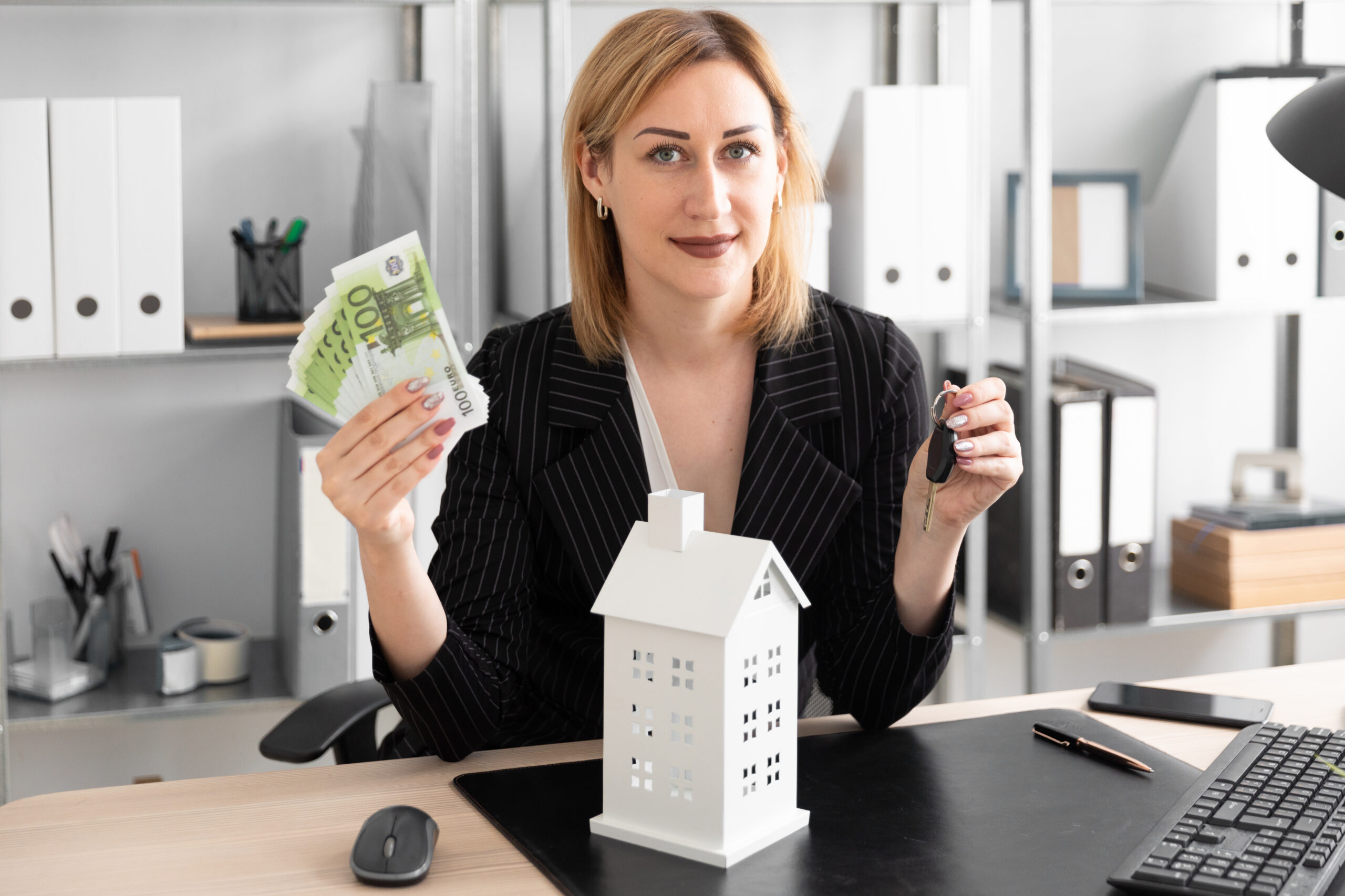 Young woman holding money with house keys placed on a table, representing home buying and financial planning