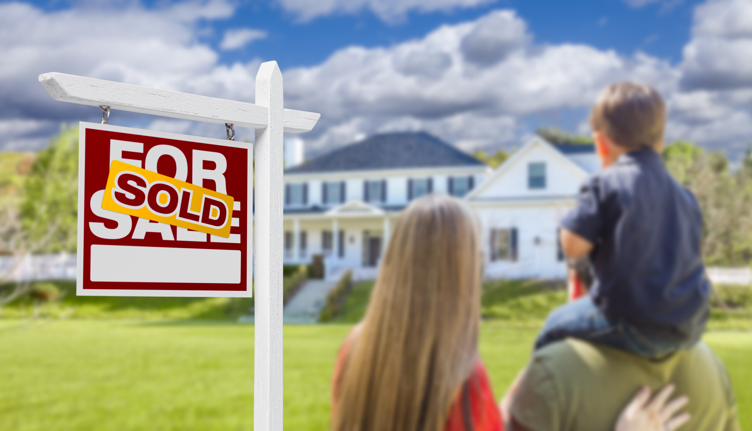 Family standing in front of a house with a "Sold" real estate sign, representing a successful home sale