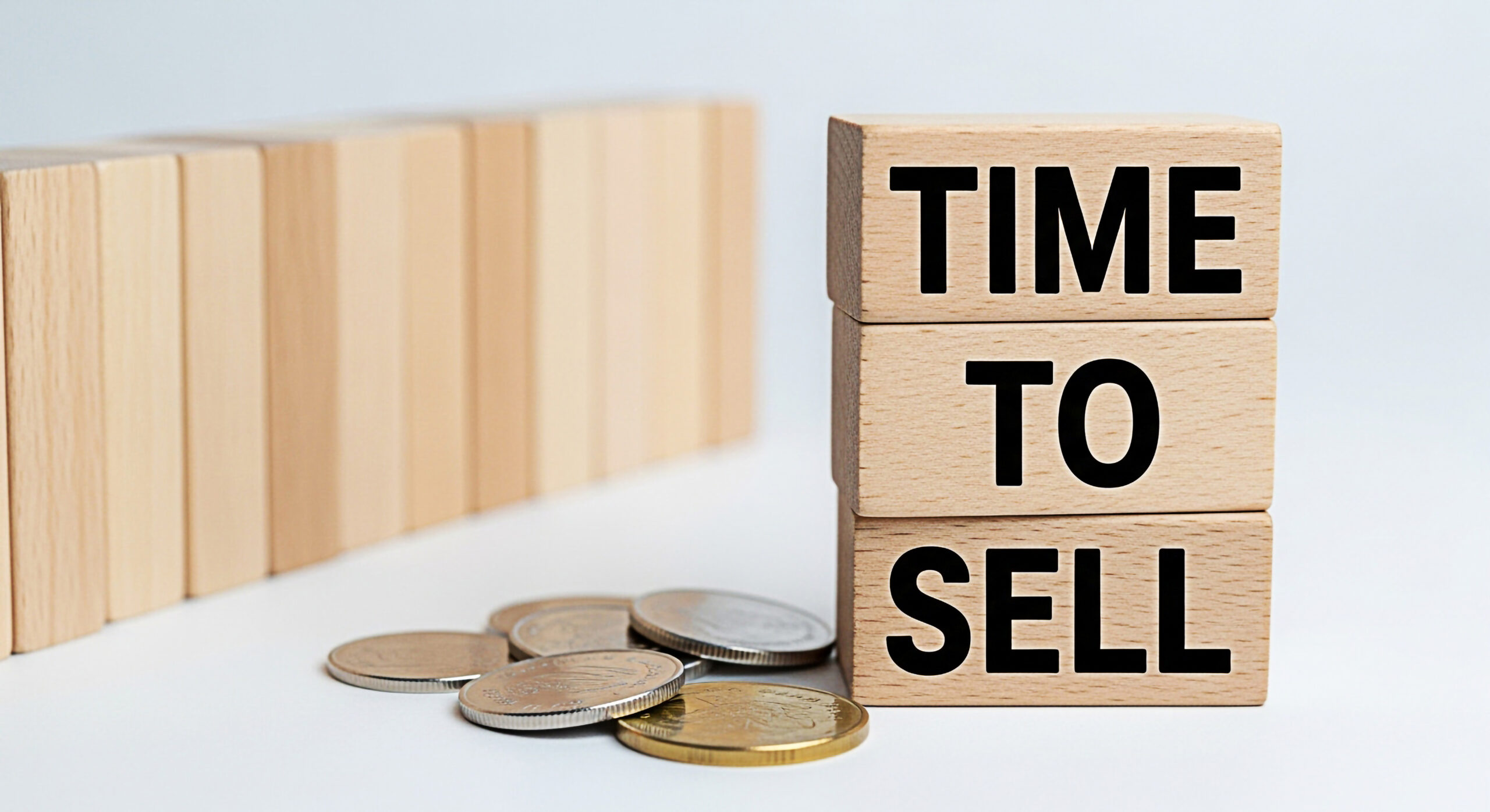 Wooden blocks spelling "TIME TO SELL" stacked with coins, symbolizing property sales and financial decisions