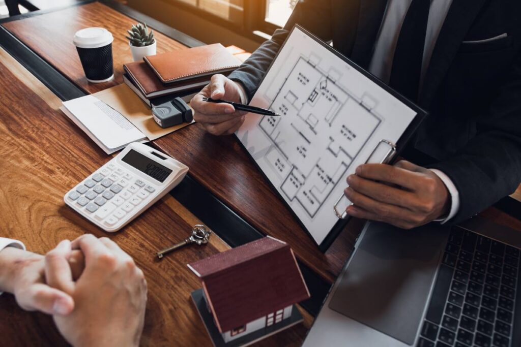 Real estate agents pointing at a home blueprint during a property discussion.