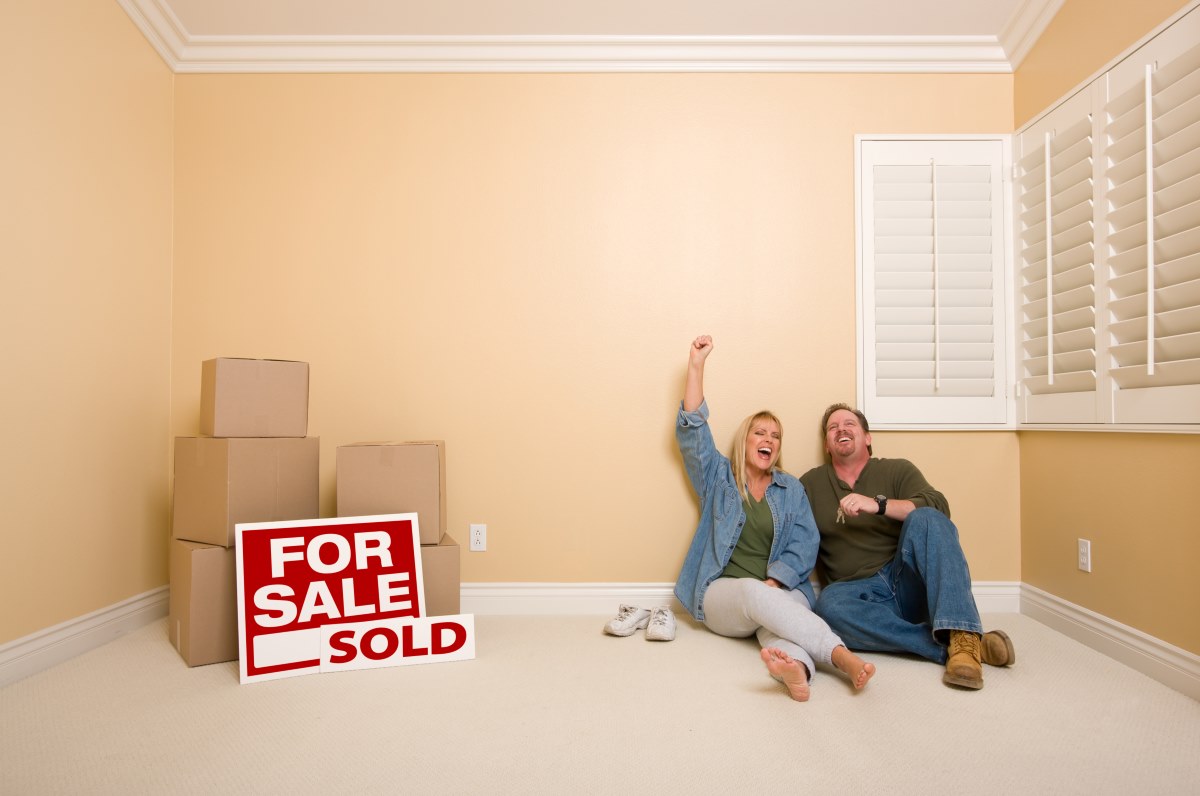 Couple sitting on the floor near moving boxes and sold real estate signs.