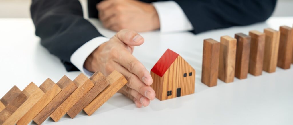 Hands protecting dominoes, representing insurance and risk protection.