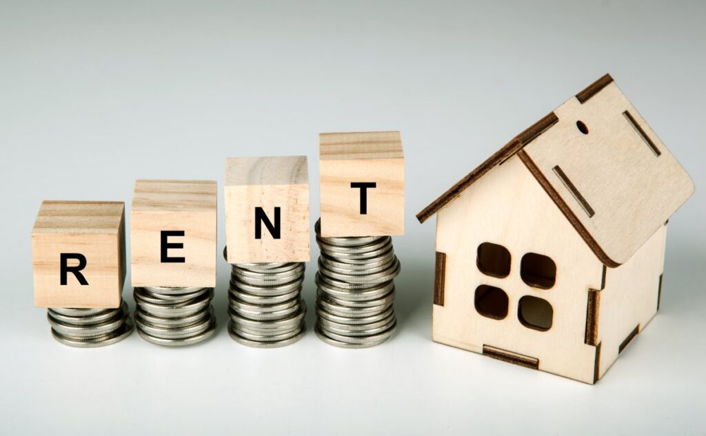 Miniature house beside wooden blocks displaying the word “Rent.”