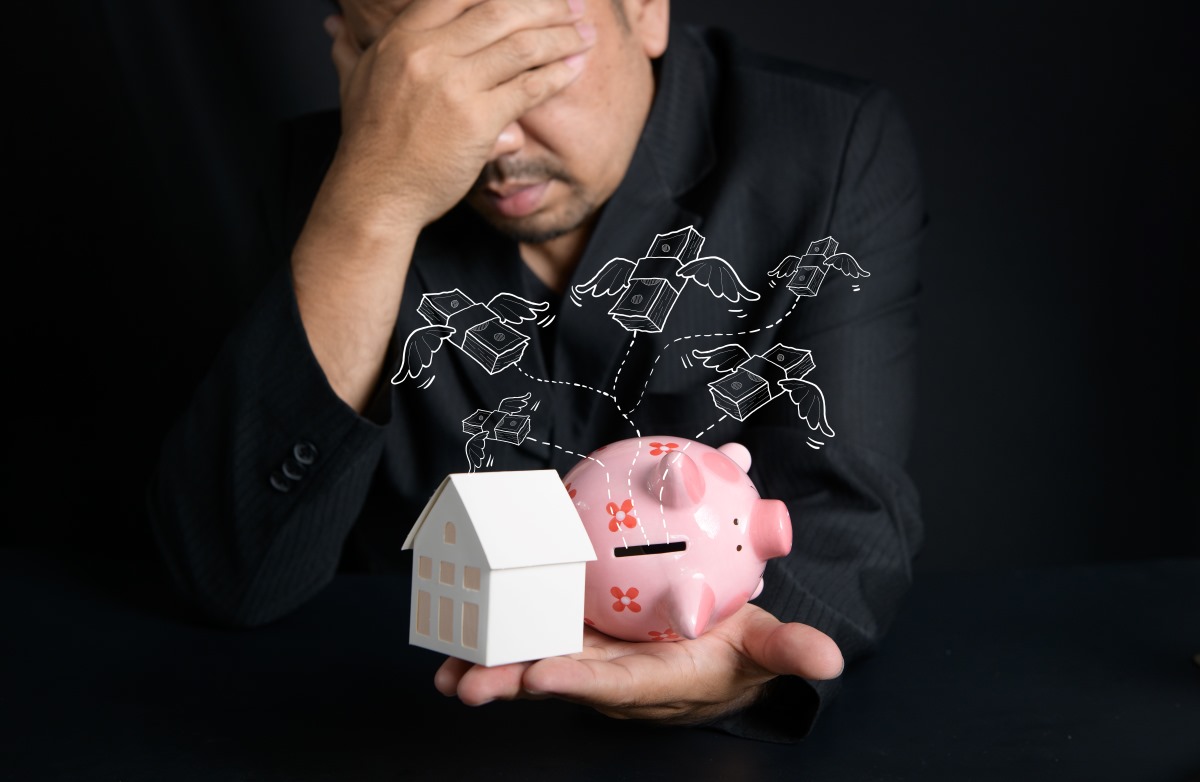 Paper house and piggy bank resting on a hand against a black background.