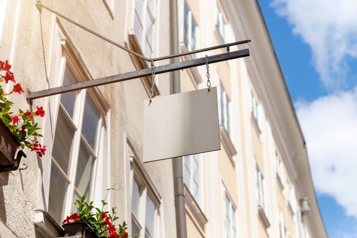 Hanging square shop sign with floral decor and sunny sky, ideal for boutique branding mockups