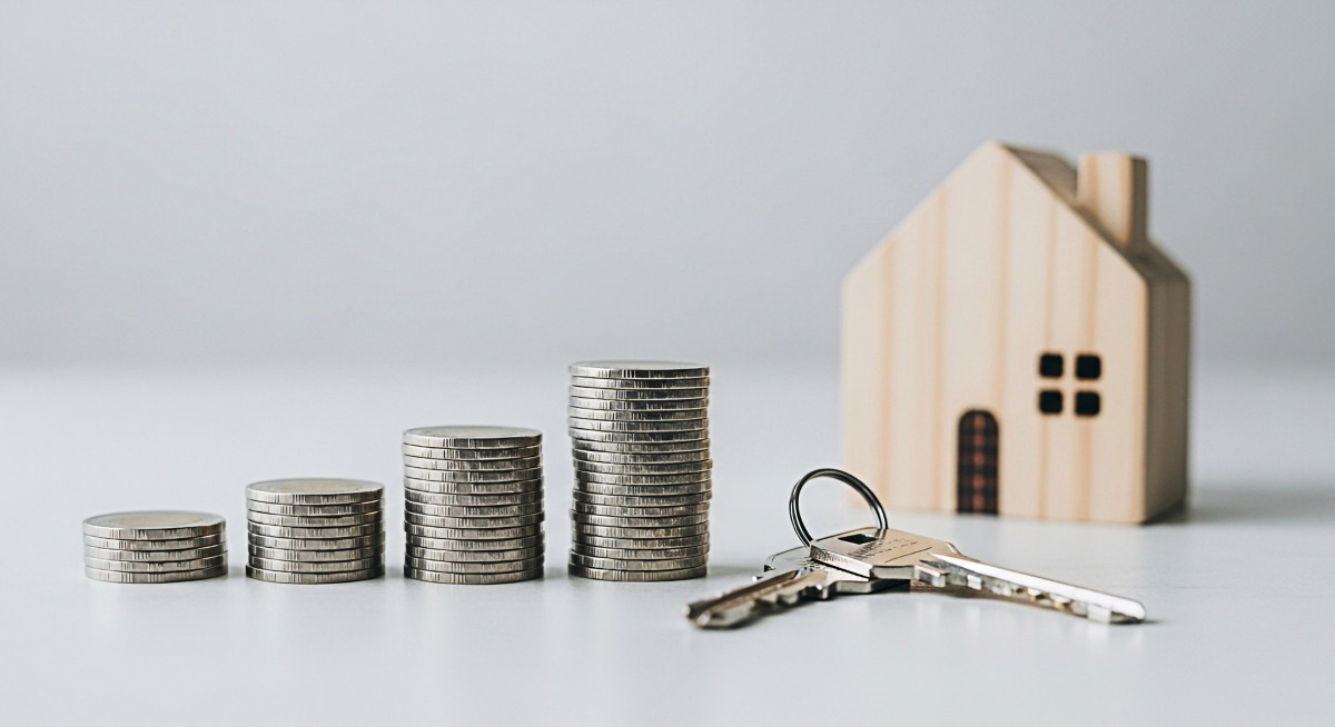 Stacks of coins and house keys on a white surface representing financial growth and investment in real estate symbolizing home ownership