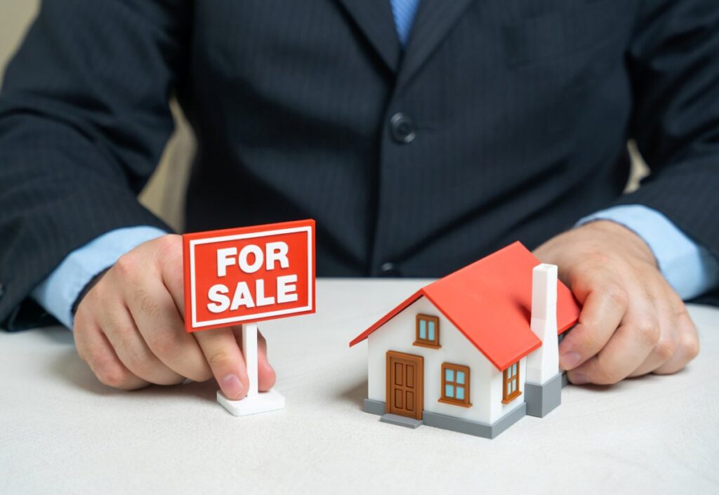 The house is up for sale. For sale sign and house in the hands of a realtor