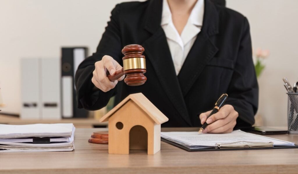 Female Lawyer Reviewing Legal Contract Documents at Desk with Gavel and House Model in Office