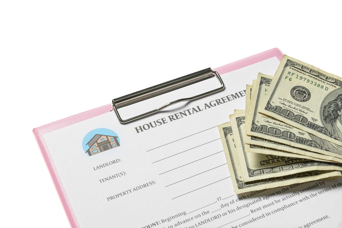 Clipboard with house rental agreement and money on white background, closeup