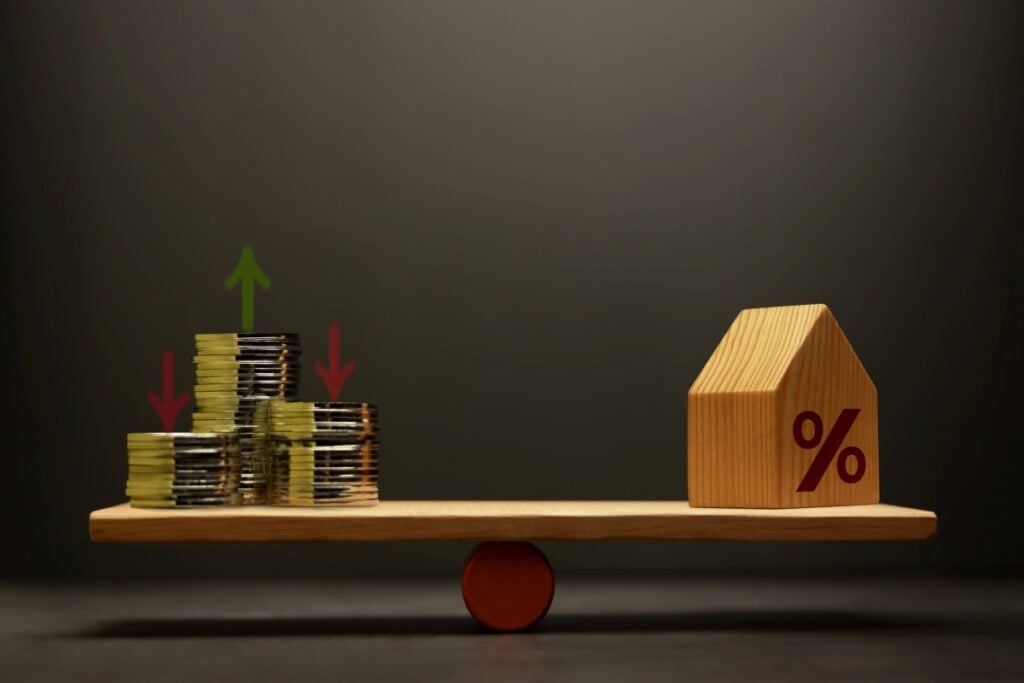 Stacked coins money and houses balanced on a scale seesaw. Mortgage interest rates