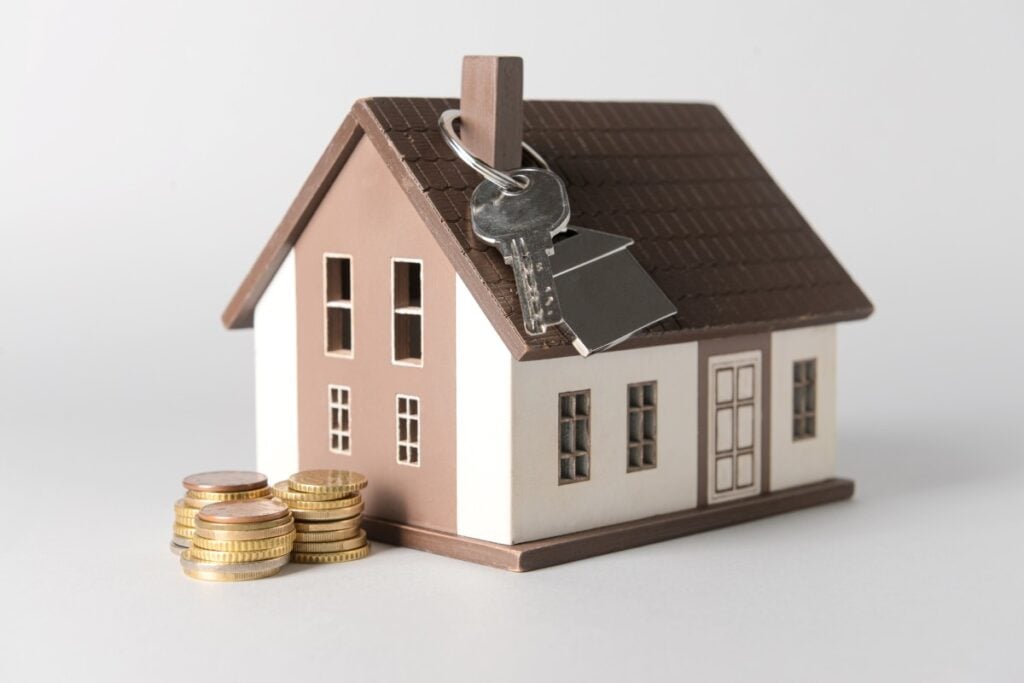 House model with key and coins on light background