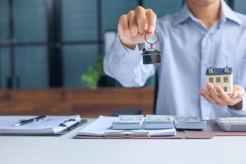 Real estate agent holding house model and hand over house keychain with money and document on the table for home ownership concept
