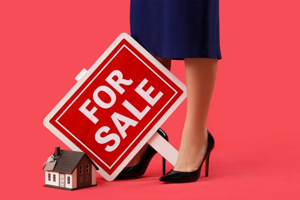 Female real estate agent with FOR SALE sign and house model on red background